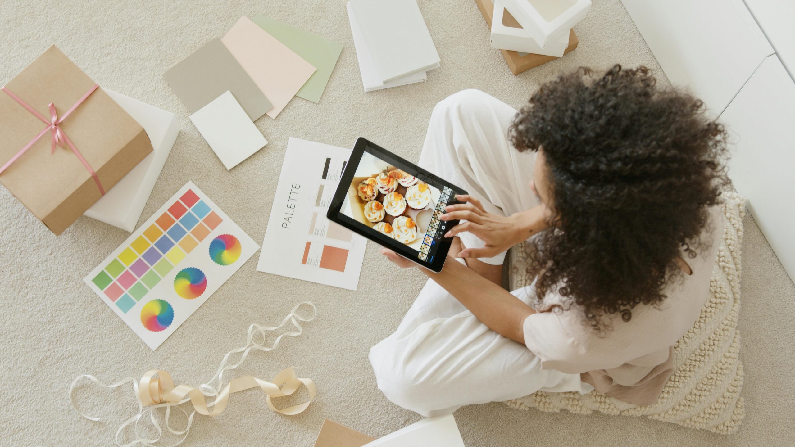 Woman sits on floor with tablet, packing orders to ship and updating her business digital marketing